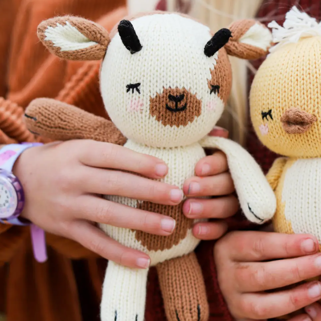 Knitted deer toys held by a child with a blurred background