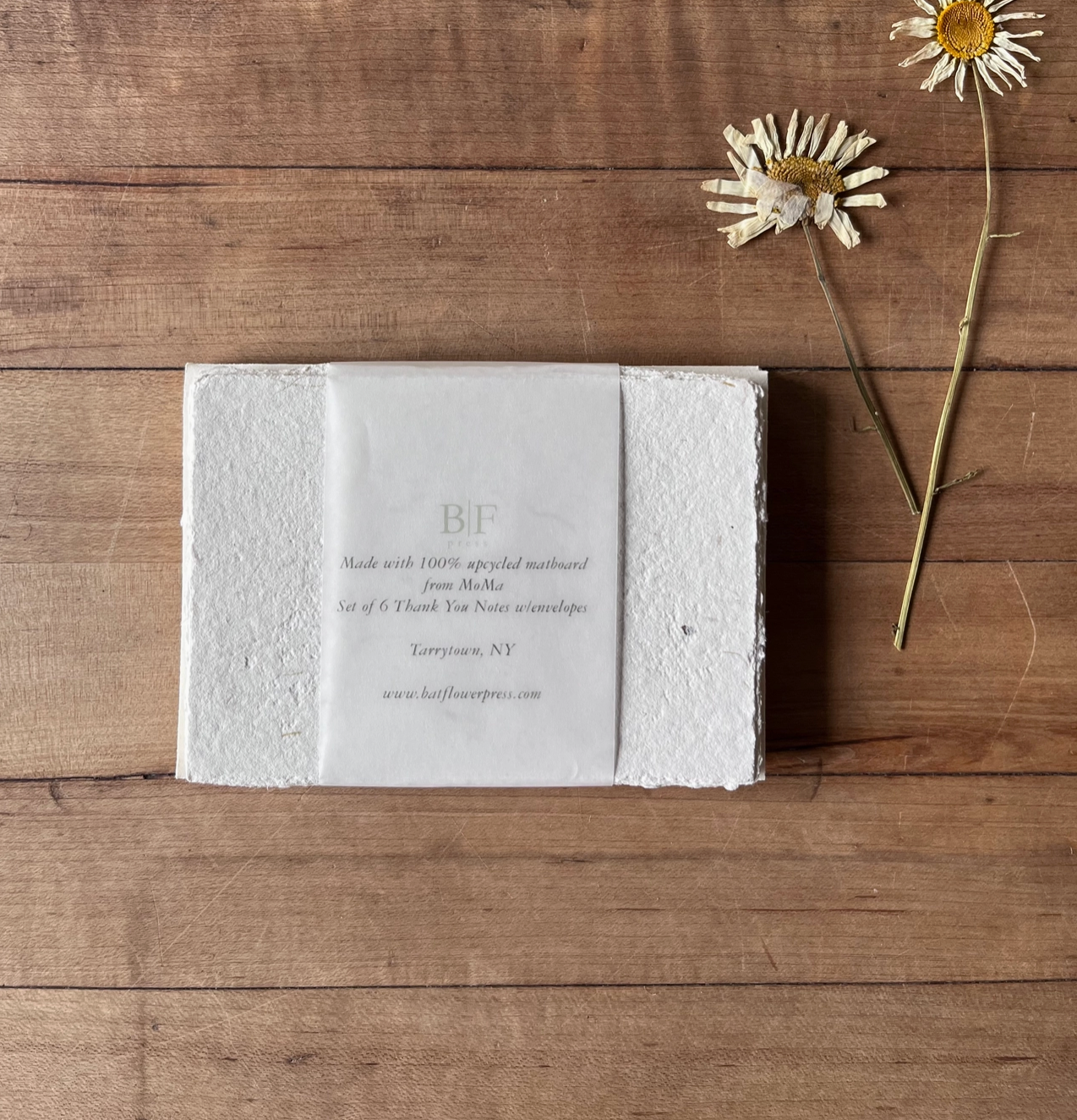 White textured box with text on a wooden surface with flowers