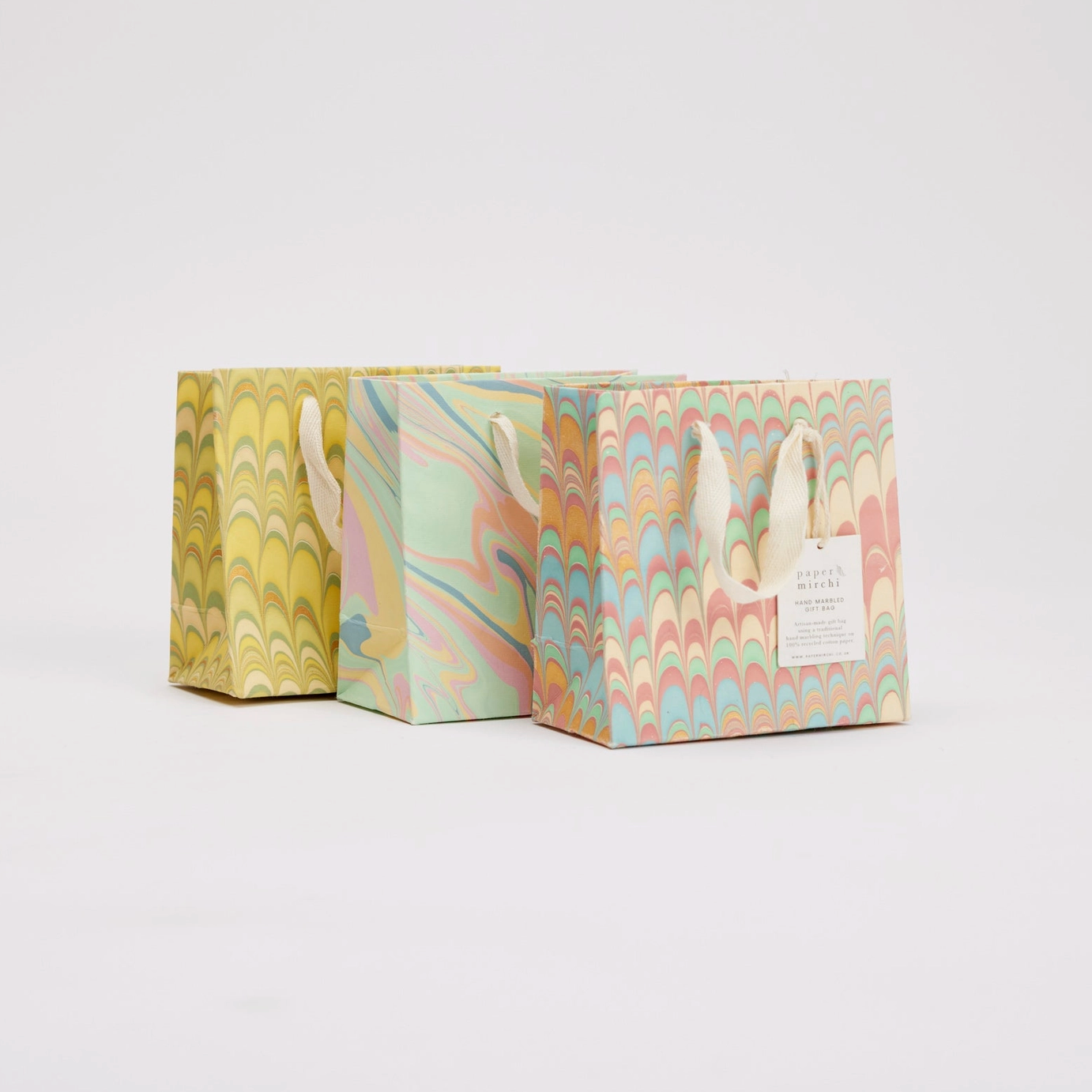 Three pastel marbled gift bags with handles on a light gray background