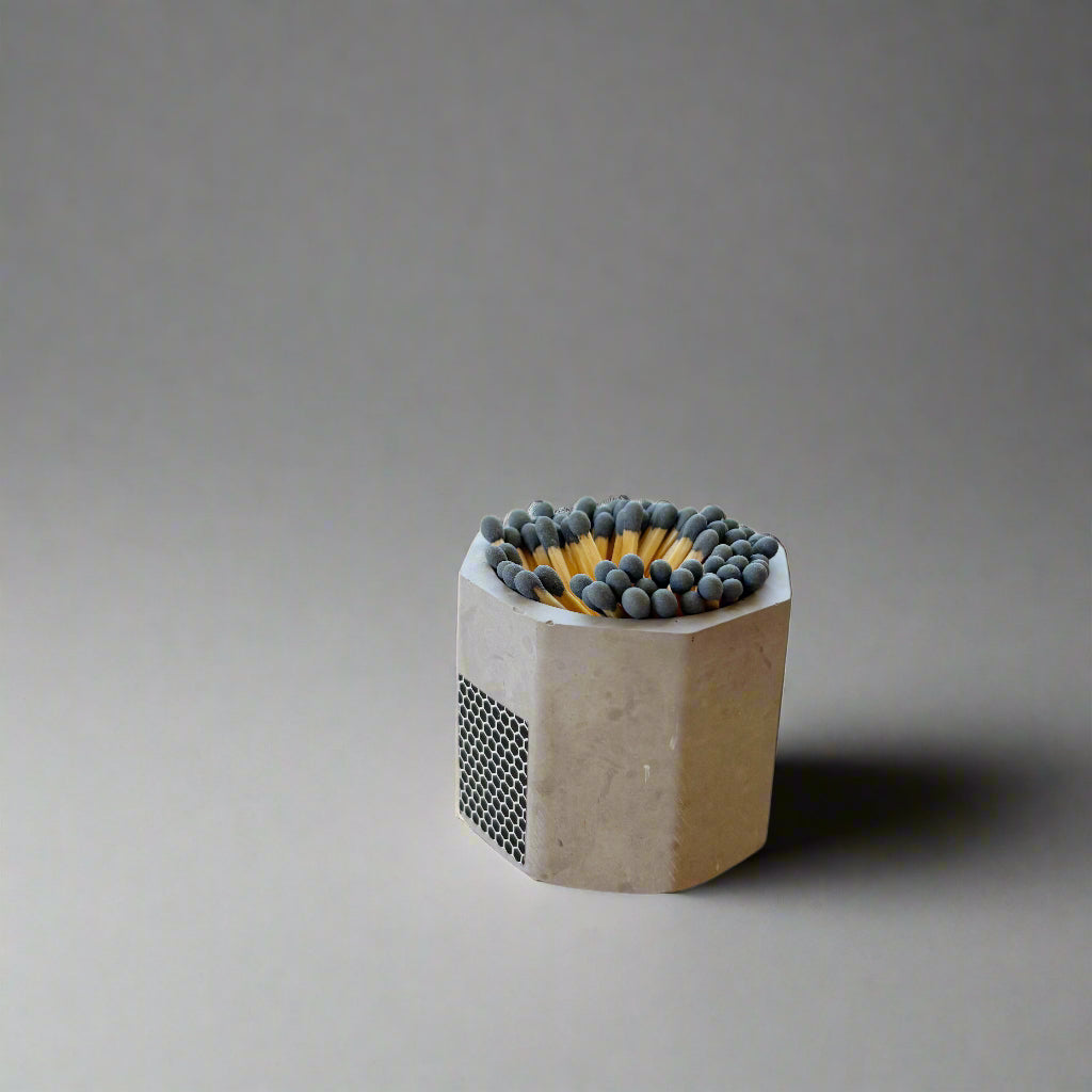 Concrete matchbox holder with matches on a wooden surface near a window.