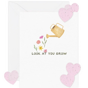 Greeting card with watering can, flowers, and hearts on a white background