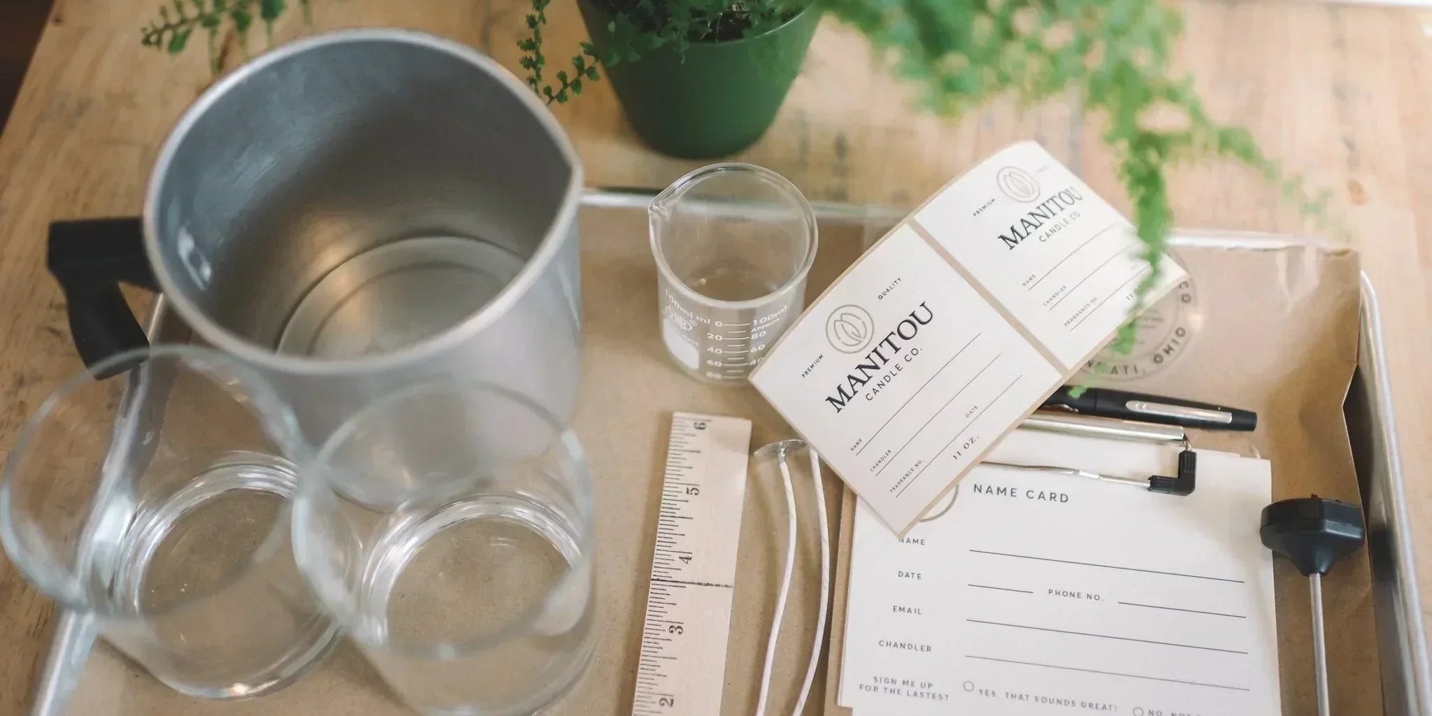 A photo capturing the setup of a candle making class with various materials laid out on a table, including glass jars, wicks, and label templates.