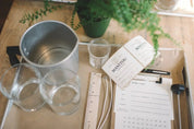 A photo capturing the setup of a candle making class with various materials laid out on a table, including glass jars, wicks, and label templates.