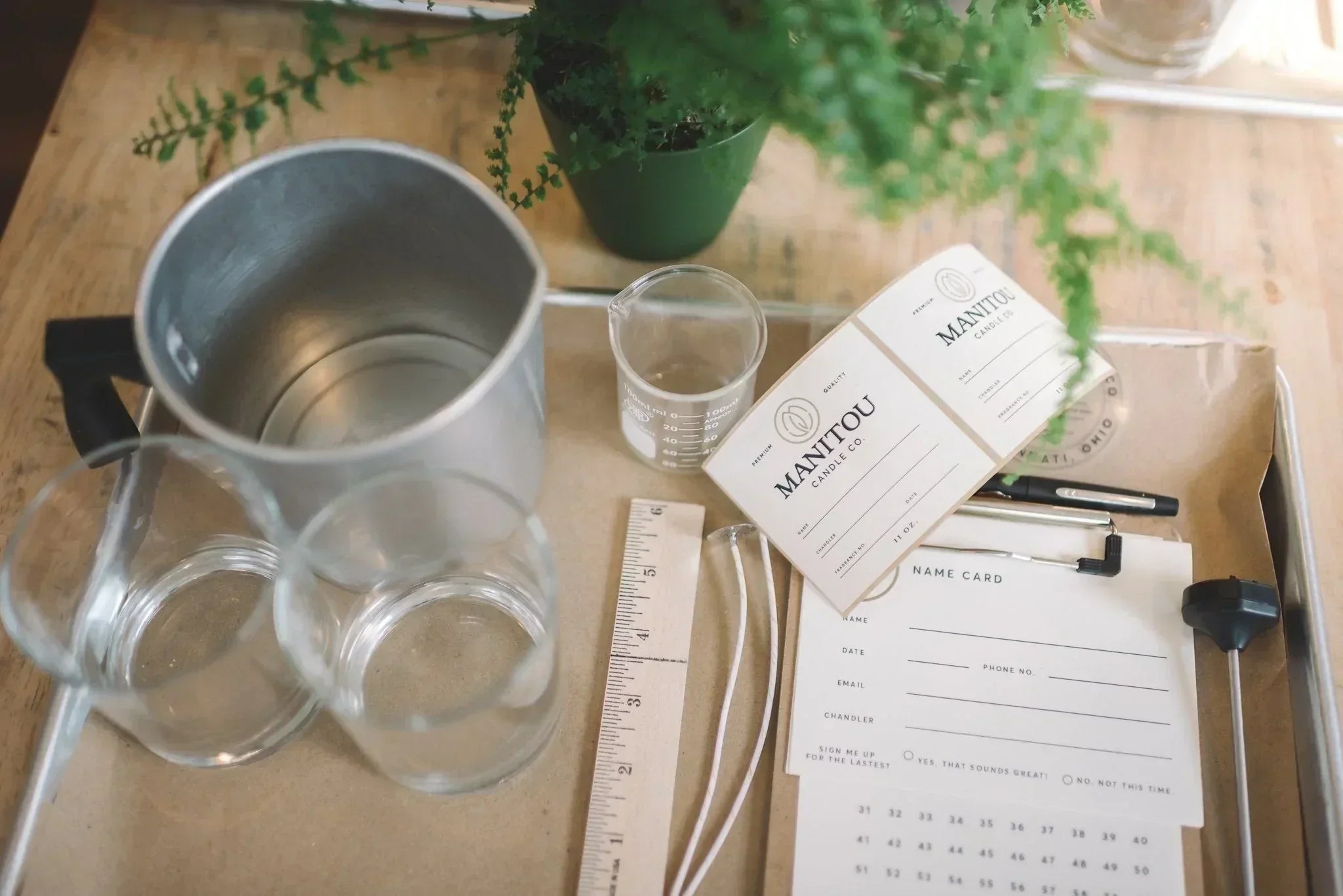 A photo capturing the setup of a candle making class with various materials laid out on a table, including glass jars, wicks, and label templates.