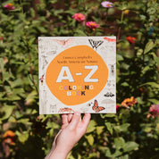 Book titled 'A-Z Coloring Book' held in front of a natural background with greenery and flowers.