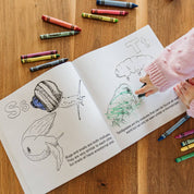 Child coloring in a book with crayons on a wooden table