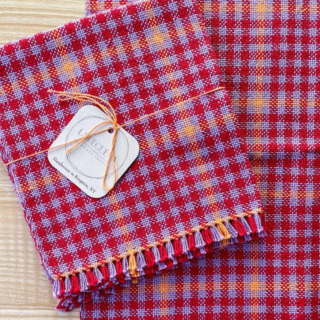 Red and lavender checkered fabric with tassels on a wooden surface