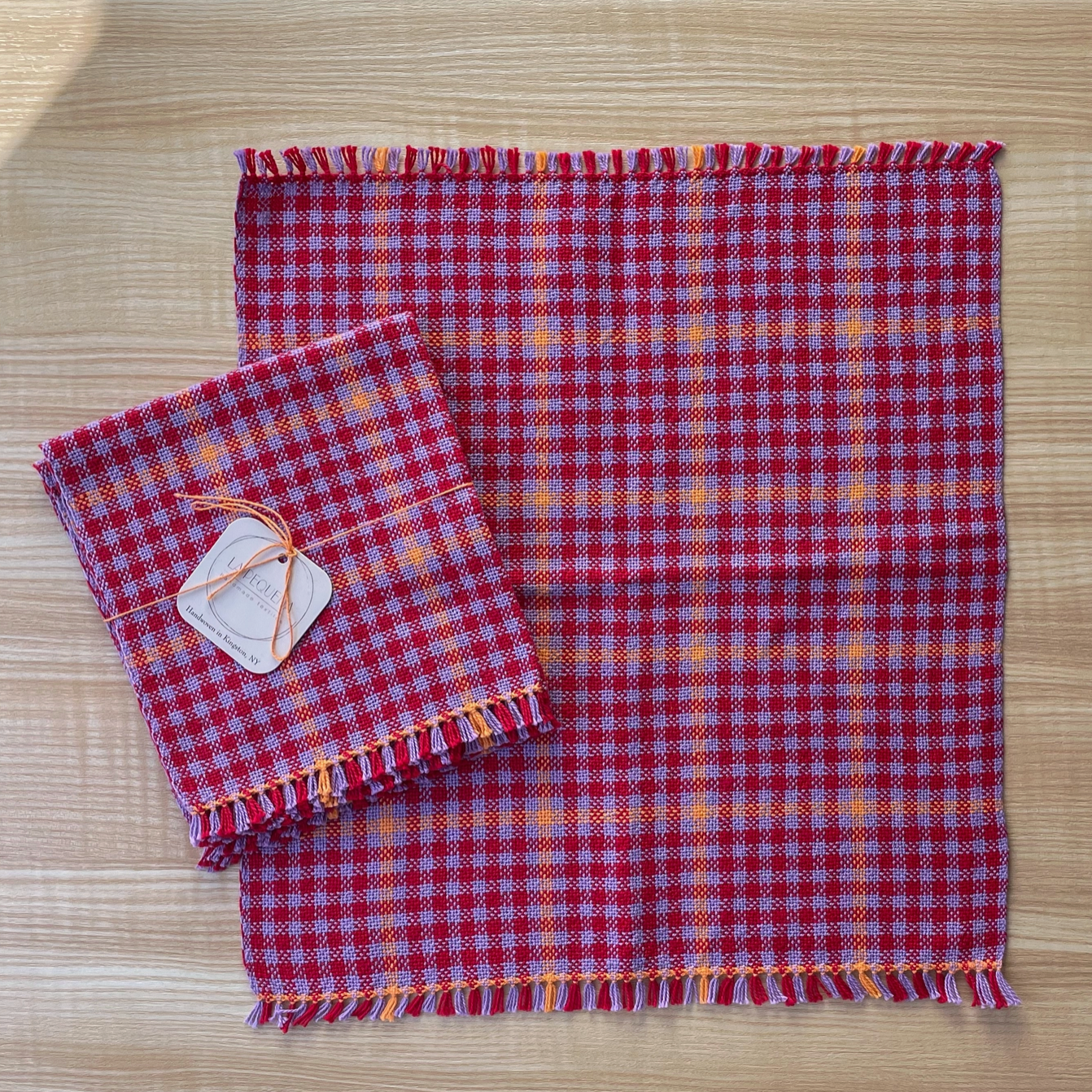Red and lavender checkered fabric with frayed edges on a wooden surface