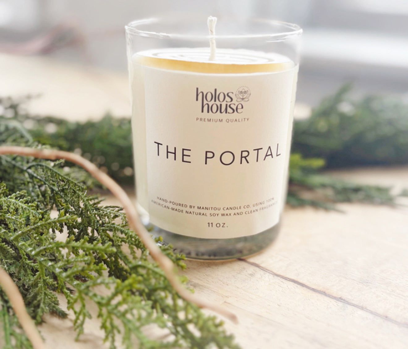 Candle with 'holos house' branding and 'The Portal' label on a wooden surface with greenery.