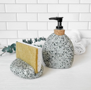 Speckled soap dispenser and dish on a bathroom counter with a white tiled wall background.