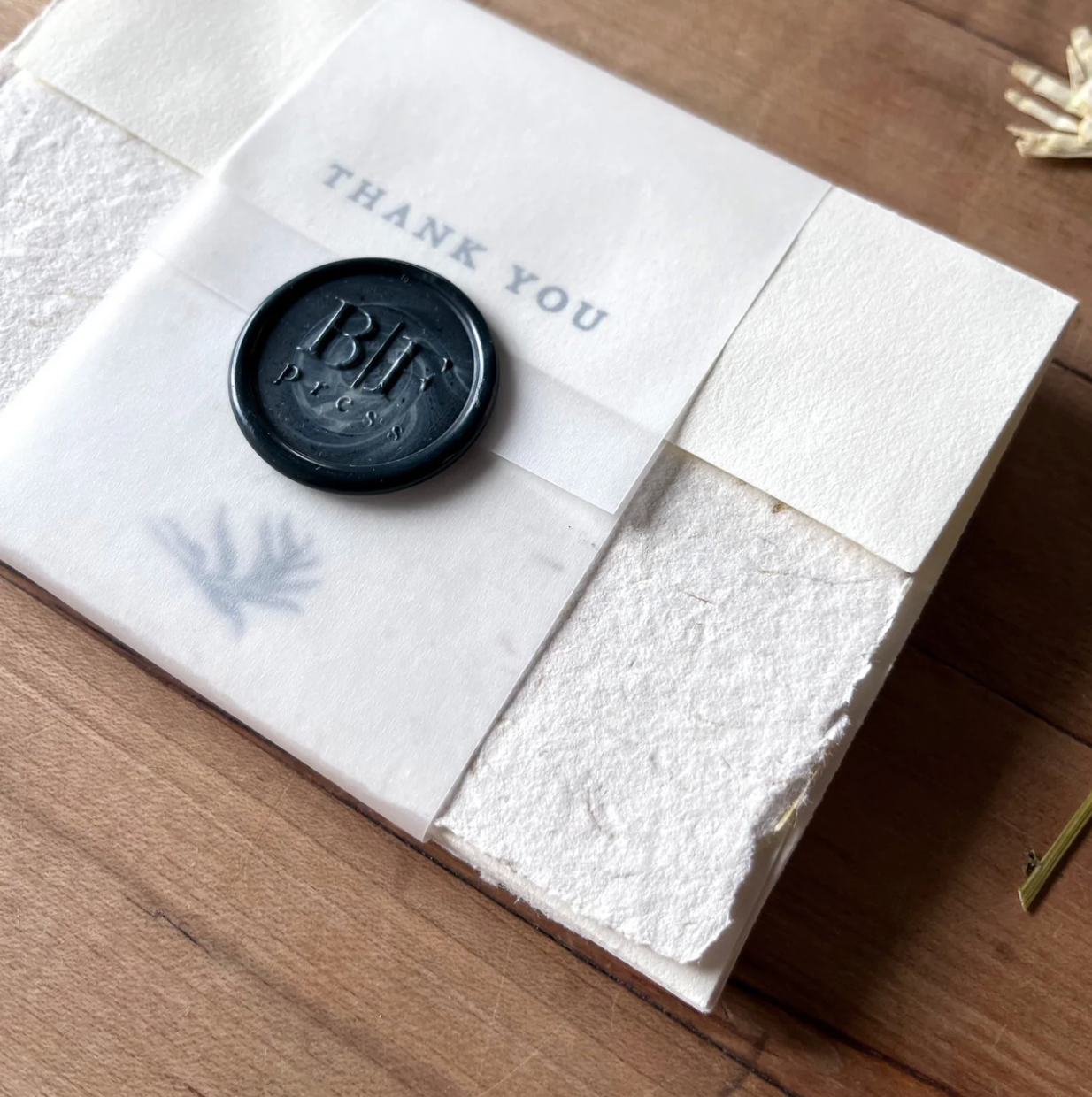 White textured card with a black wax seal and 'THANK YOU' text on a wooden surface