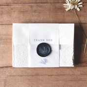White card with 'Thank You' message and black wax seal on wooden surface